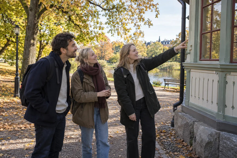 Tre vuxna vänner stannar under en parkpromenad och pekar ut en detalj på en byggnad för varandra.